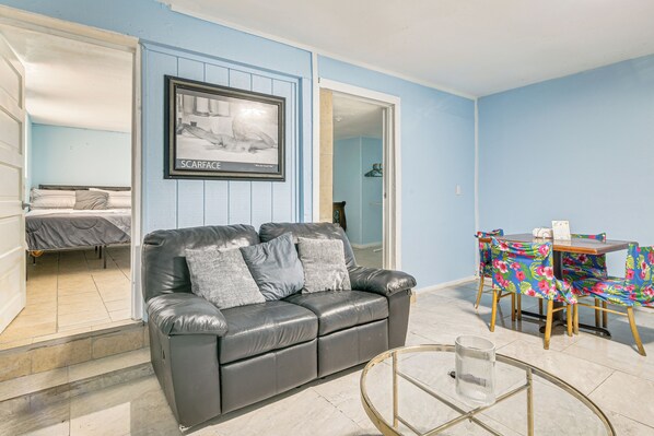 A room with a black leather sofa, a glass coffee table, and a dining table with a floral tablecloth. - Gateway to Downtown Harlingen! Quaint Unit (Harlingen)