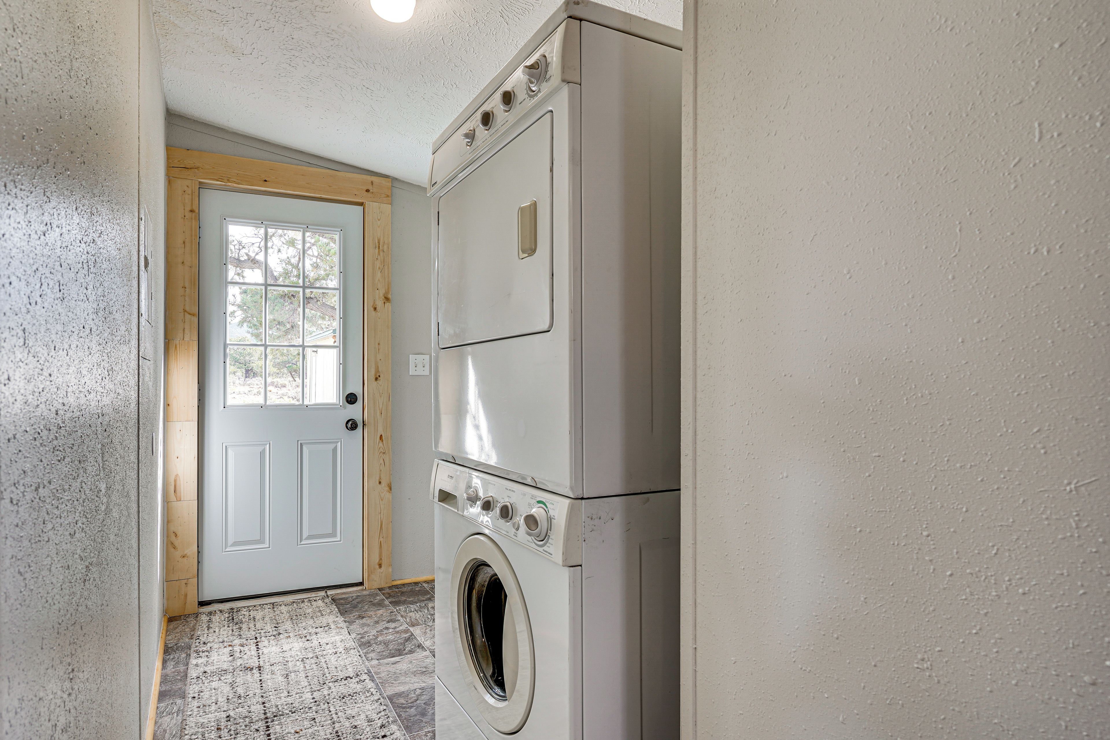 A laundry room with a front-loading washer and dryer, a wooden door, and a textured wall.
