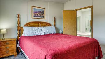 A bedroom with a wooden bed, a nightstand with a lamp, a framed picture on the wall, and a wooden door leading to a bathroom.