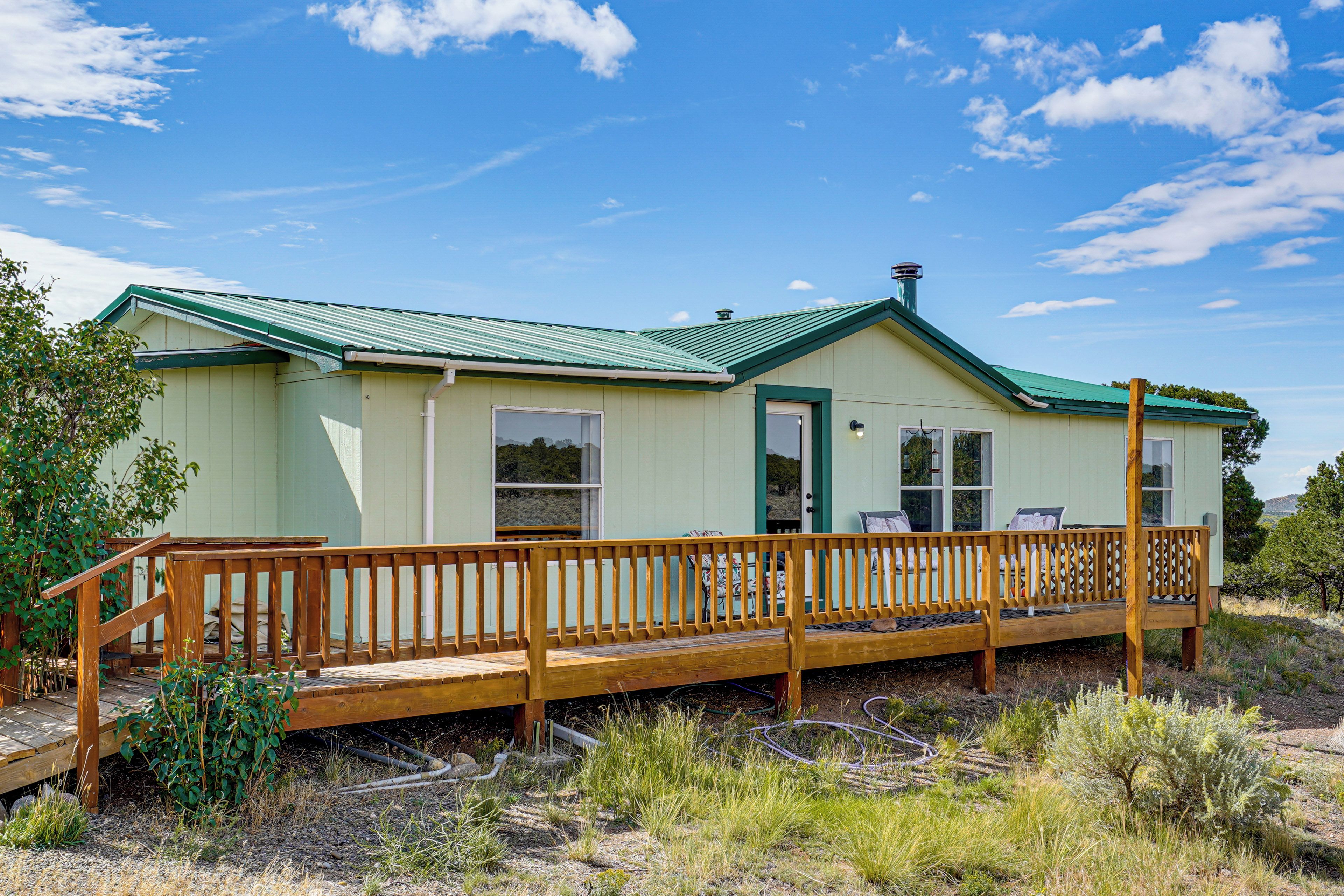 A single-story house with a green roof, a wooden deck, and a door.