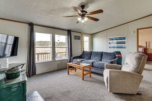 A living room with a ceiling fan, a television, a sofa, a coffee table, and a view of the outdoors through large windows. - Colorado Getaway at the Base of Sangre de Christos (Fort Garland)