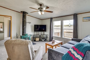 A cozy living room with a television, a ceiling fan, and a view of the outdoors through large windows.