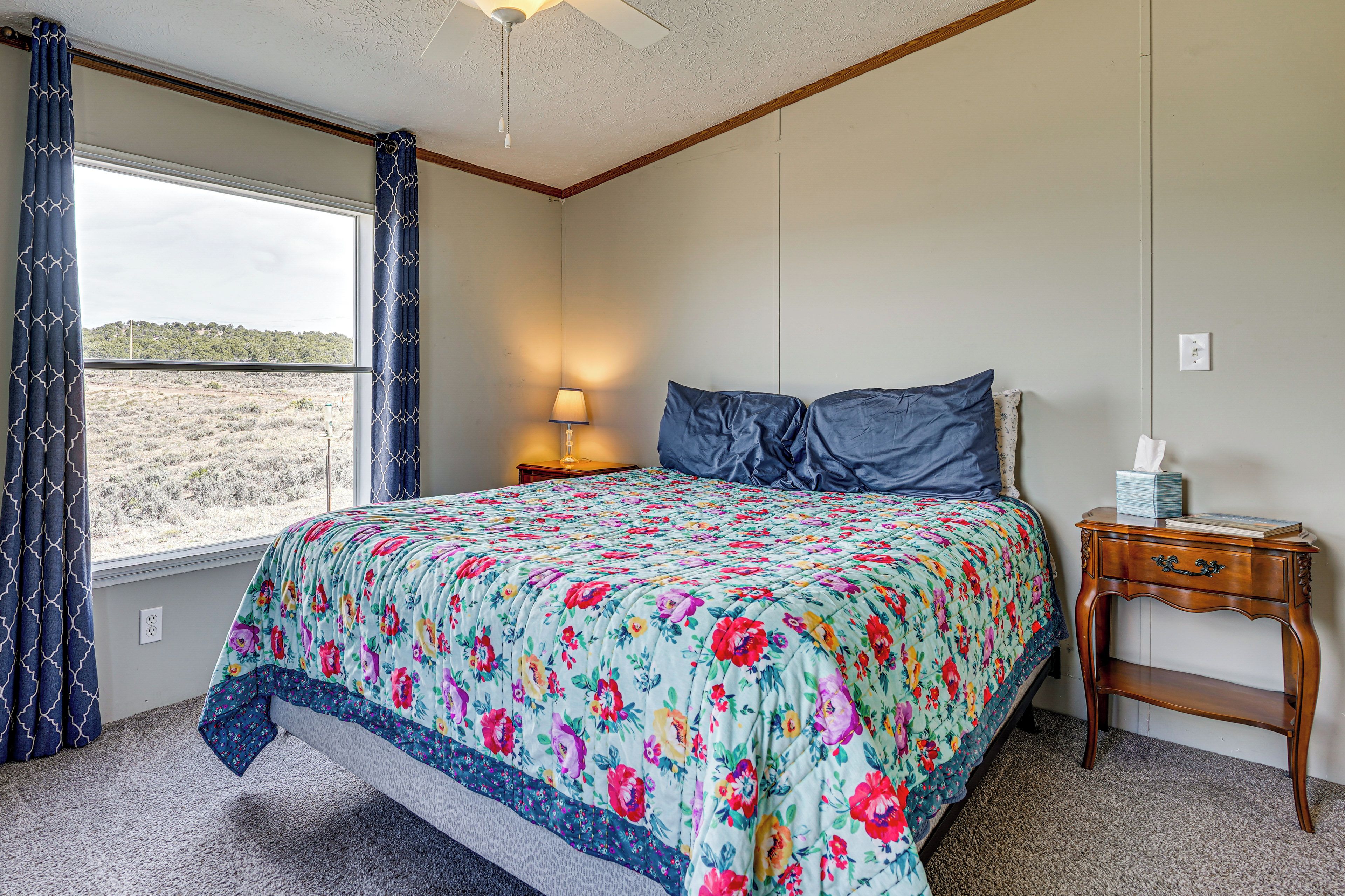 A bedroom with a bed, a nightstand, a lamp, a window with curtains, and a view of a landscape.