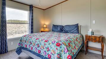 A bedroom with a bed, a nightstand, a lamp, a window with curtains, and a view of a landscape.