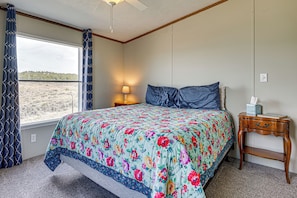Un dormitorio con cama, mesita de noche, lámpara, ventana con cortinas y vistas al paisaje.