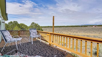 A wooden deck with two chairs and a table, overlooking a dry landscape with sparse vegetation and distant mountains.