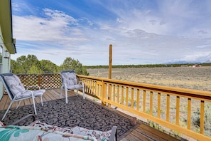 A wooden deck with two chairs and a table, overlooking a dry landscape with sparse vegetation and distant mountains.