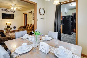 A dining area with a table set for four, a clock on the wall, and a living room in the background.