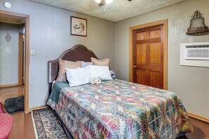 A bedroom with a bed, a wooden door, a wall-mounted air conditioner, and a patterned bedspread. - Near Dtwn Jackson: Home w/ Screened Porch (Jackson)