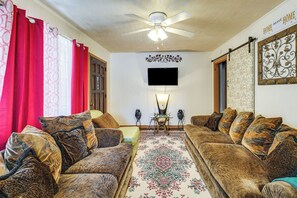 A living room with a ceiling fan, a flat-screen TV mounted on the wall, and a patterned rug.