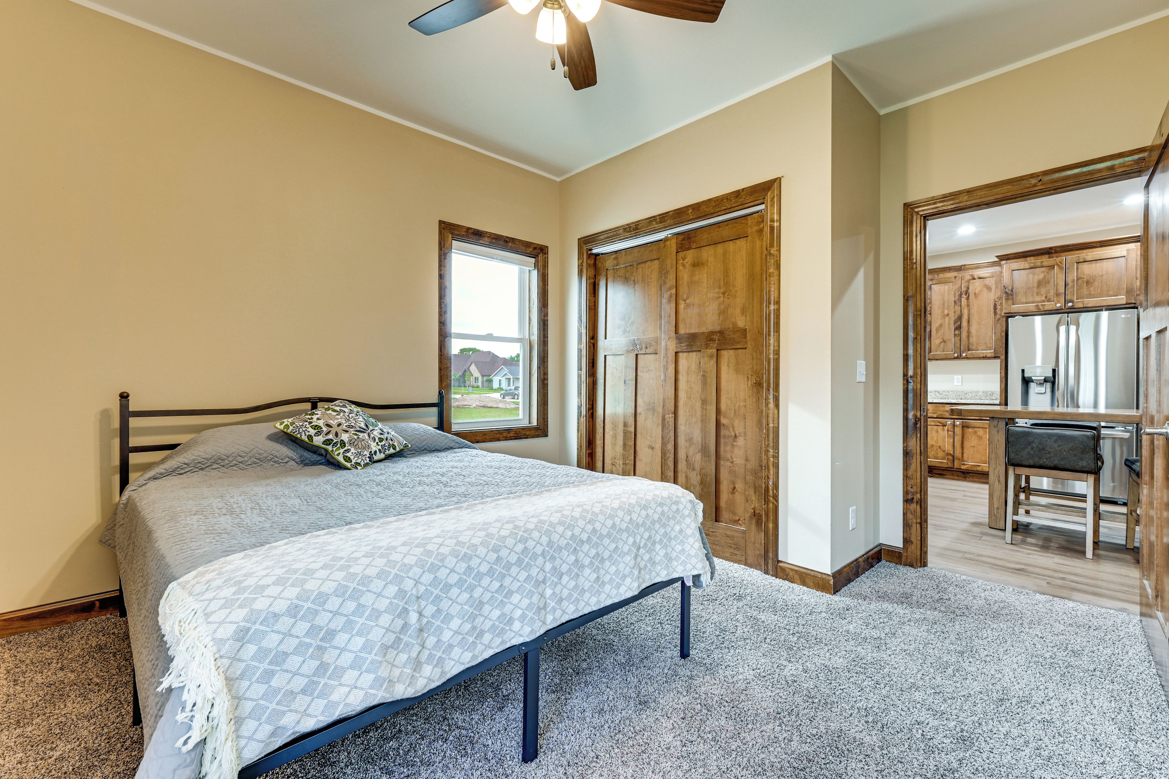 A bedroom with a bed, a window, wooden doors, and a kitchenette.