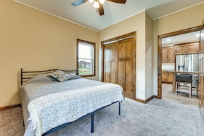 A bedroom with a bed, a window, wooden doors, and a kitchenette.
