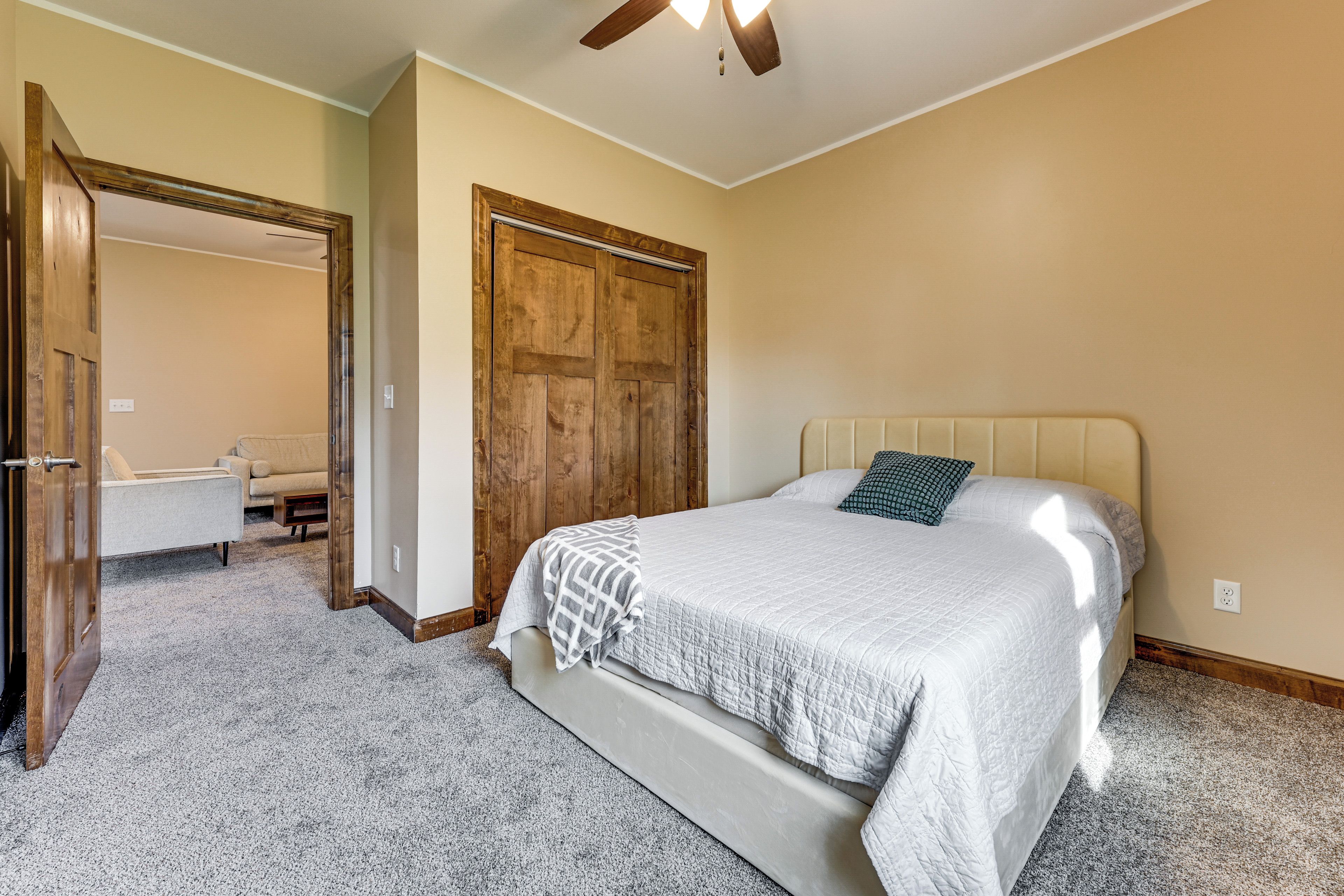 A bedroom with a bed, a wooden door, a ceiling fan, and a carpeted floor.