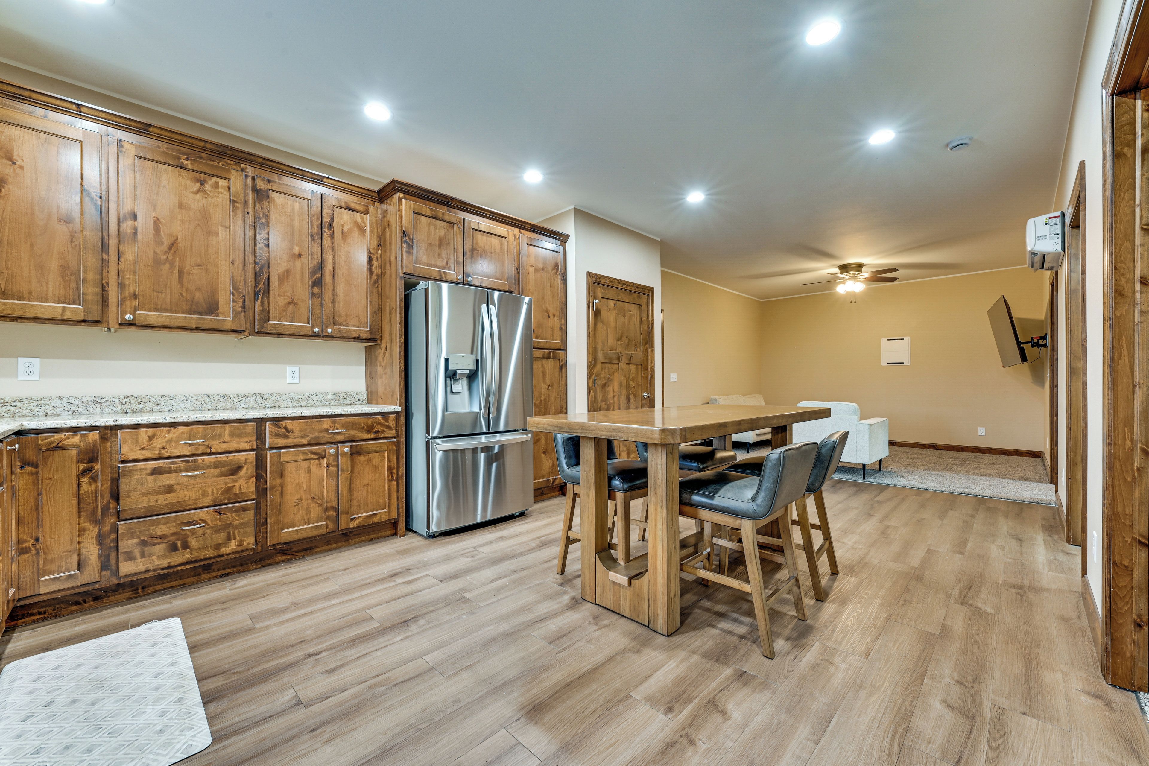 A kitchen with wooden cabinets, a stainless steel refrigerator, and a dining area with a wooden table and chairs.