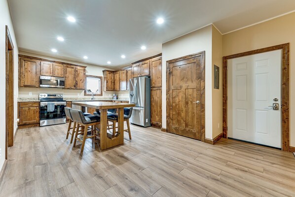 A modern kitchen with wooden cabinets, stainless steel appliances, and a bar area with stools.