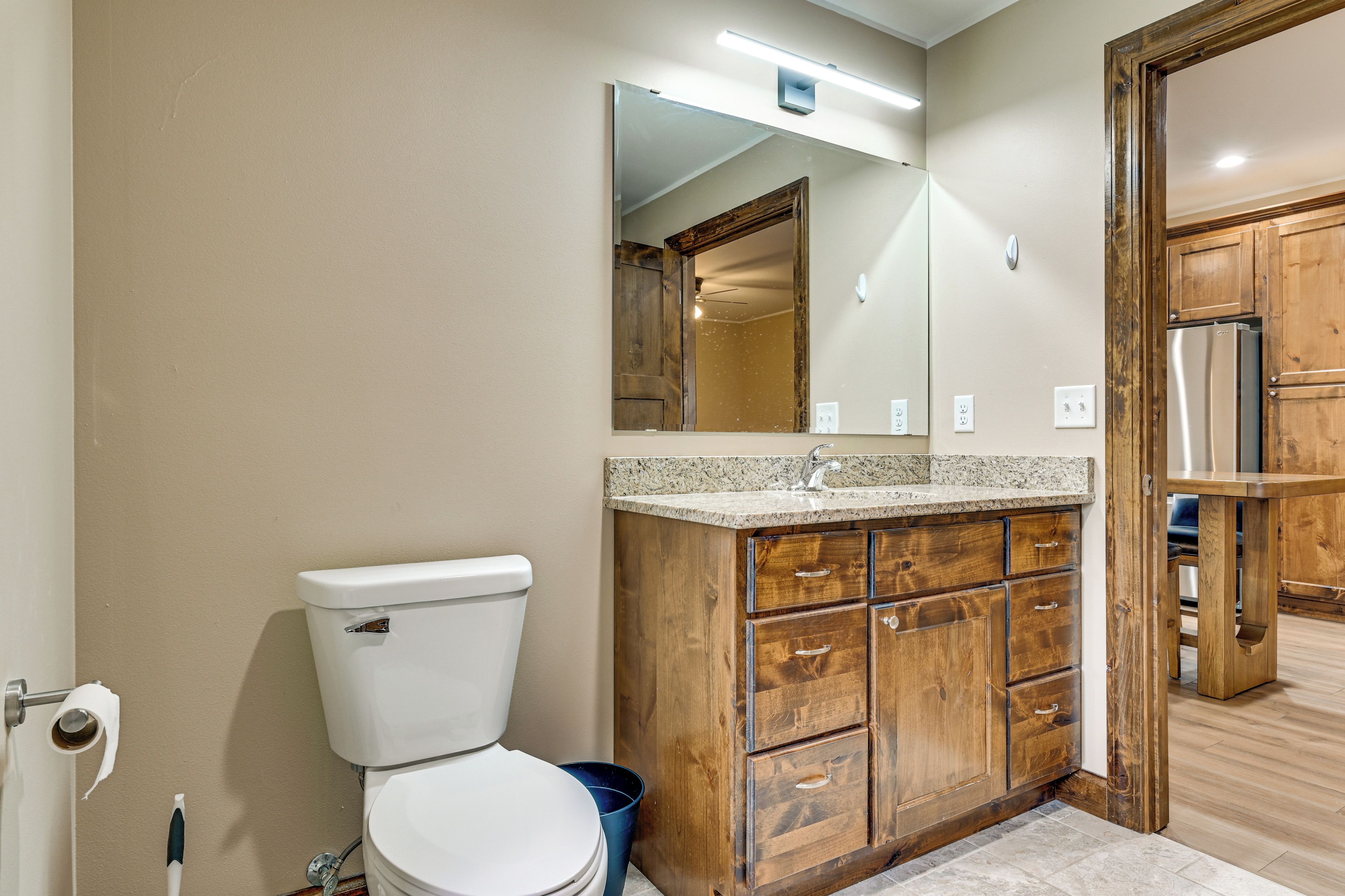 A bathroom with a toilet, wooden vanity, granite countertop, and a mirror.
