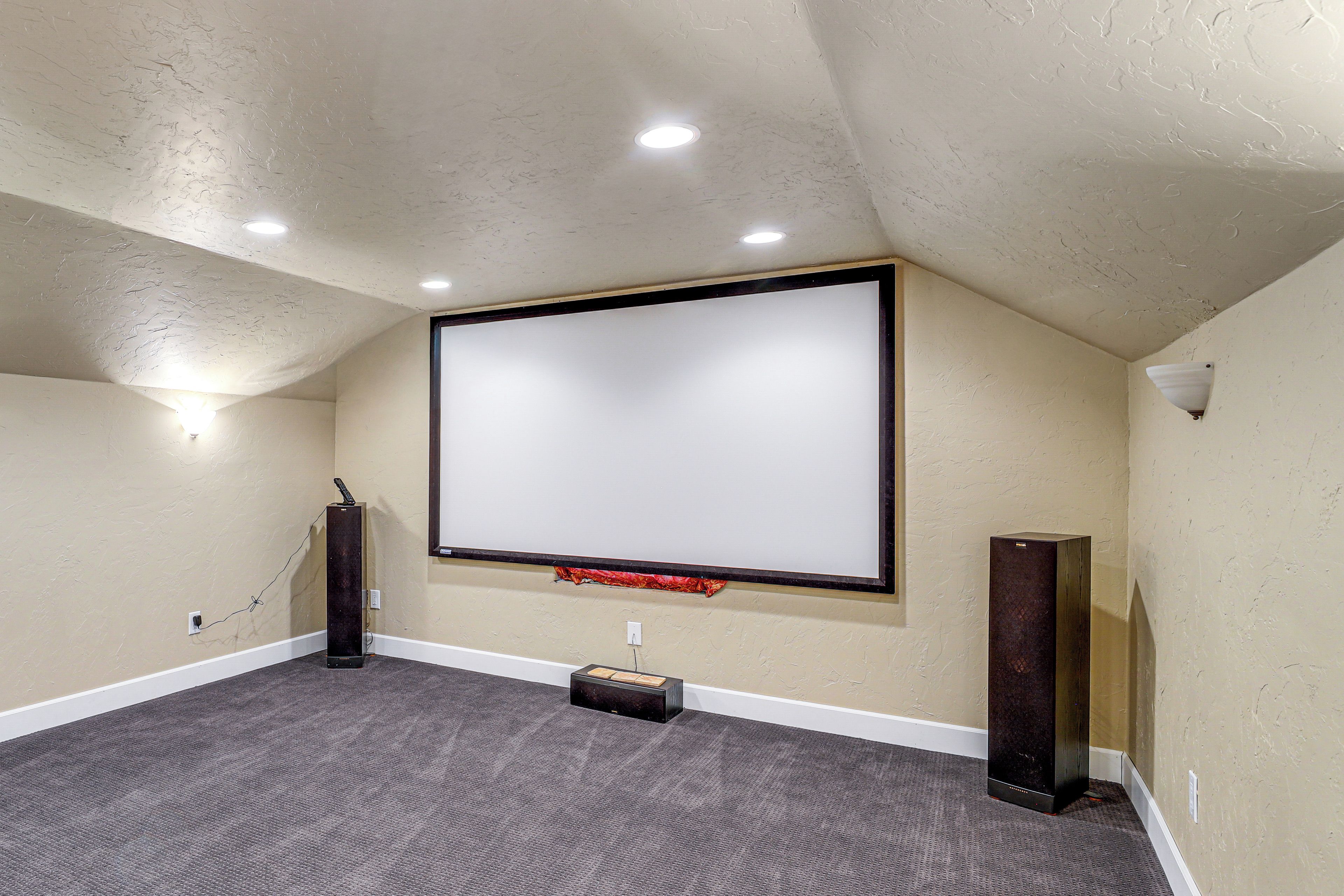 Un cine en casa con un televisor de pantalla plana grande montado en la pared, piso alfombrado e iluminación empotrada en el techo.