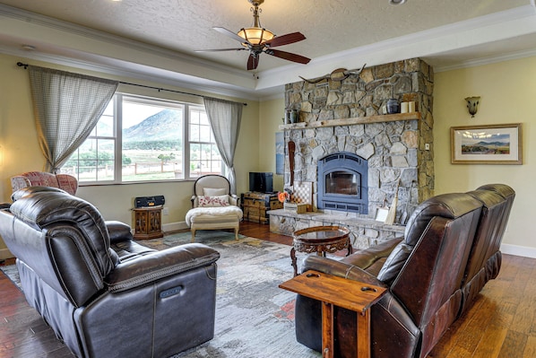 A living room with leather sofas, a stone fireplace, and a large window with curtains.