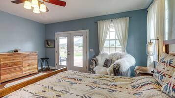 A bedroom with a large bed, a ceiling fan, a dresser, and a view of the outdoors through a door.