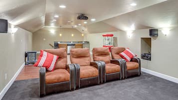 A home theater room with a seating area, a kitchen in the background, and a ceiling-mounted projector.