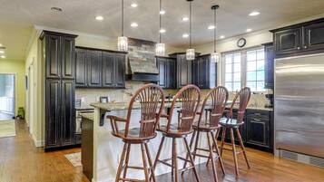 A kitchen with dark cabinets, a stainless steel refrigerator, wooden bar stools, and pendant lighting.
