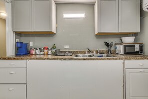 A kitchen with white cabinets, a granite countertop, a sink, a microwave, and various kitchen utensils. - Central Rio Grande Valley Hub w/ Full Kitchen! (La Feria)