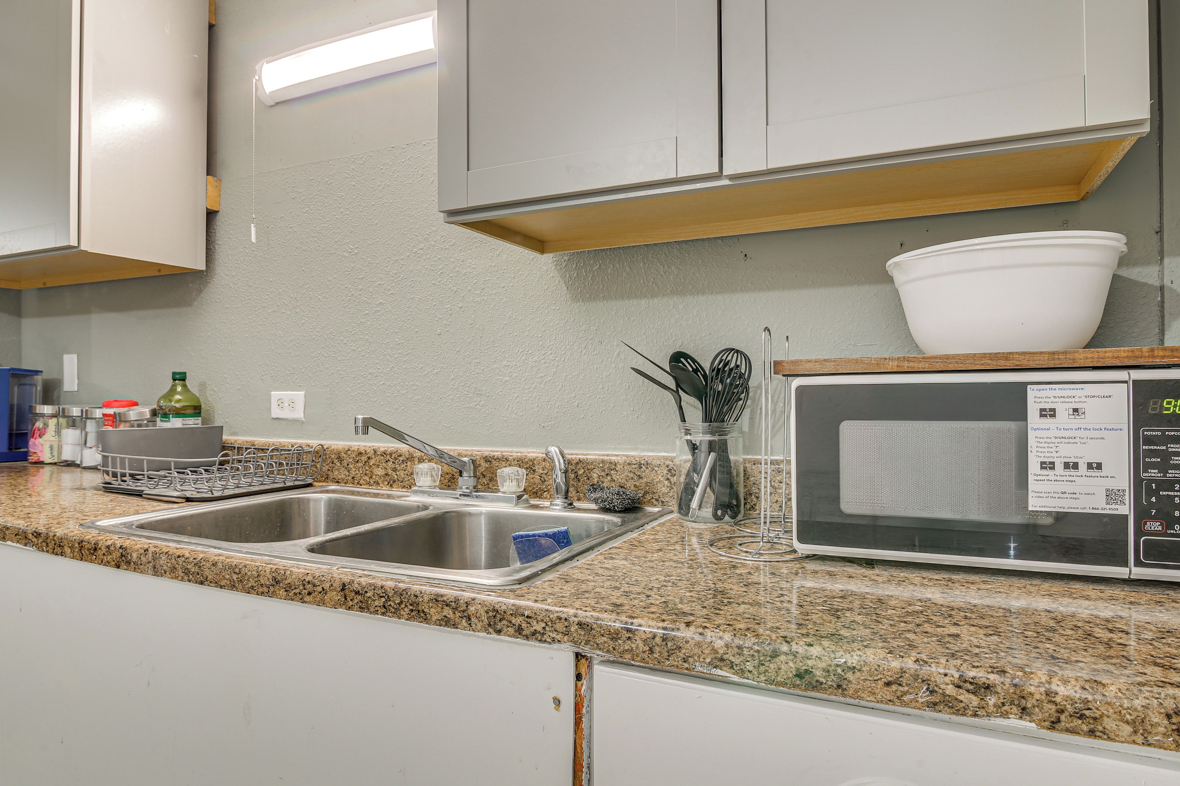 A kitchen with a granite countertop, stainless steel sink, and a microwave.