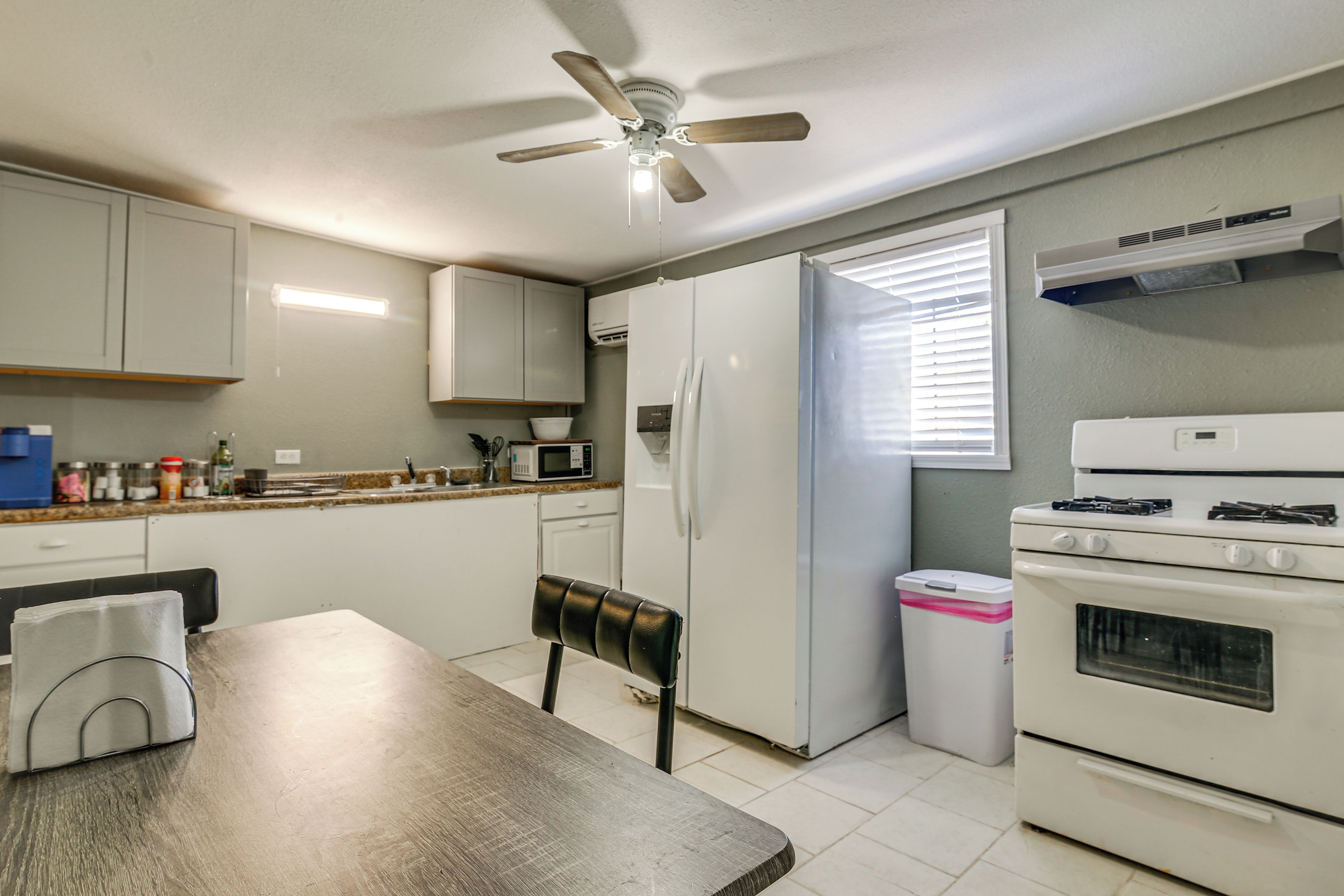 A compact kitchen with a dining table, chairs, a ceiling fan, a refrigerator, a microwave, and an oven.