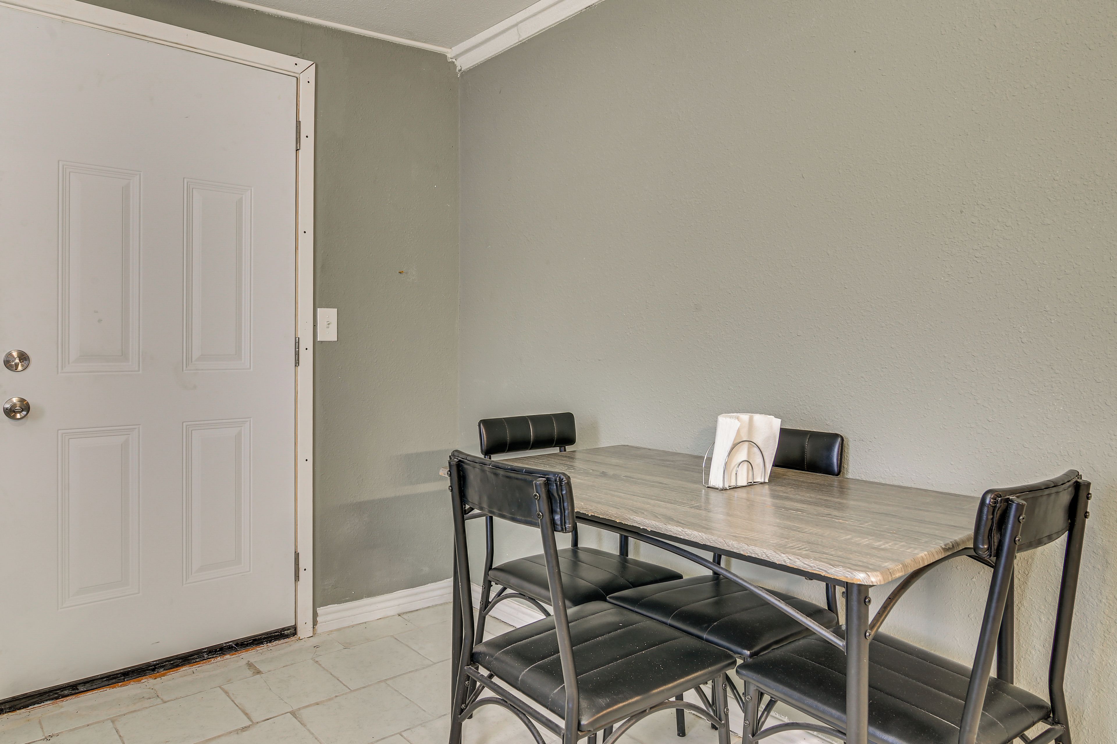 A dining area with a table and four chairs, a white door, and a light-colored wall.