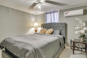 A bedroom with a bed, a nightstand, a lamp, a ceiling fan, a window with curtains, and an air conditioning unit. - Central Rio Grande Valley Hub w/ Full Kitchen! (La Feria)