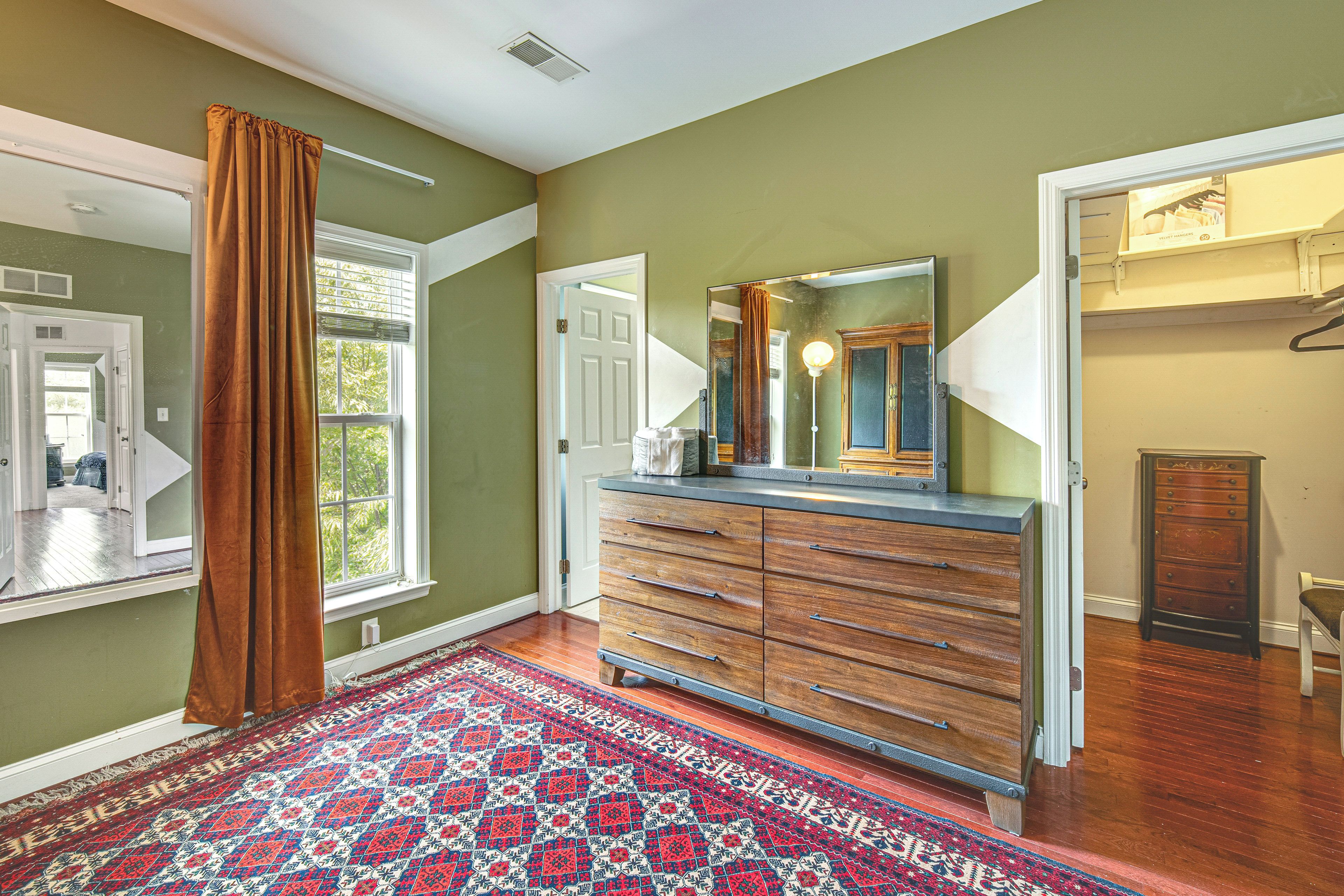 A hallway with a patterned rug, wooden dresser, and a mirror.