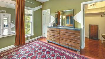 A hallway with a patterned rug, wooden dresser, and a mirror.