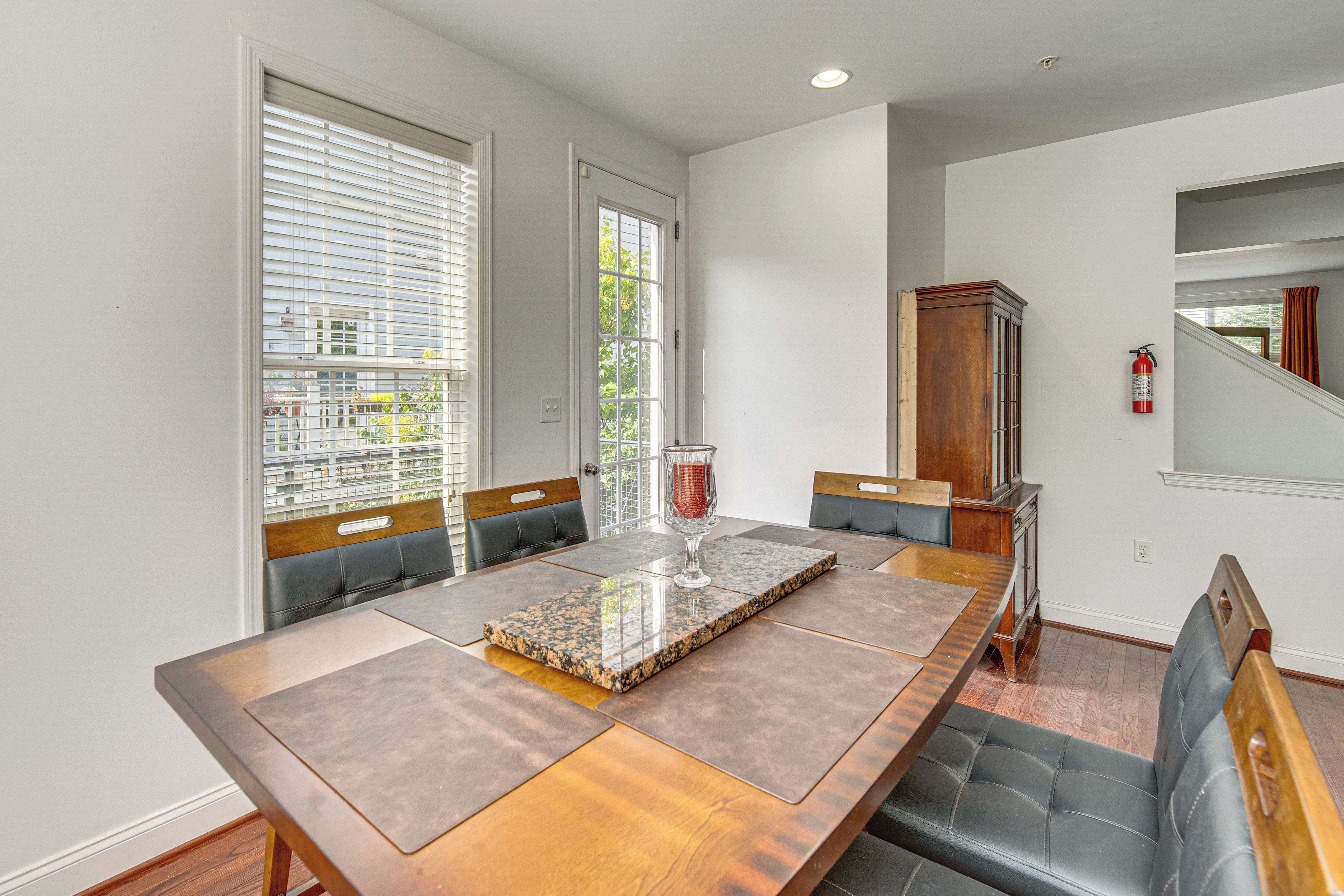 A dining area with a long wooden table, cushioned chairs, and a glass vase centerpiece.
