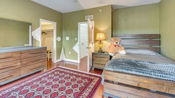A bedroom with a bed, a dresser, a lamp, a teddy bear, and a patterned rug.