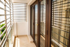 Un balcon doté d’une rambarde en métal, d’une porte vitrée et offrant une vue sur la verdure.