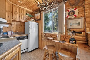 Eine Küchenzeile im Blockhausstil mit Holzschränken, einem Kühlschrank, einer Spüle und einem Fenster mit Blick auf einen Wald.