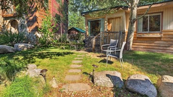 A rustic cabin with a stone pathway leading to a wooden deck, surrounded by rocks and greenery.