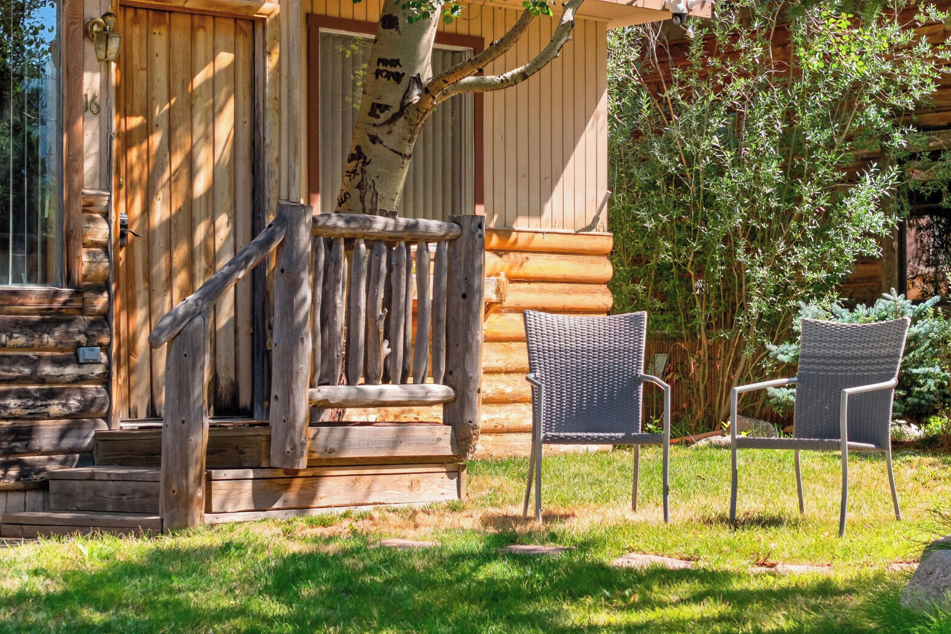Una cabaña de troncos con un porche de madera, una escalera que conduce a la entrada y dos sillas de mimbre en el exterior.
