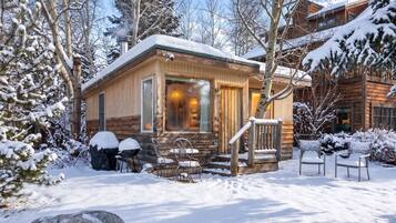 A wooden cabin with a porch, surrounded by snow-covered trees.