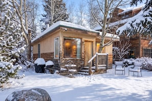 Une cabane en bois dotée d’un porche, entourée d’arbres couverts de neige.