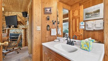 Ein Interieur einer Holzhütte mit einem großen Spiegel mit Holzrahmen, einem weißen Waschbecken und einem an der Wand befestigten Fernseher.