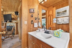 L'intérieur d'un chalet en bois, avec un grand miroir à cadre en bois, un lavabo blanc et un téléviseur fixé au mur.