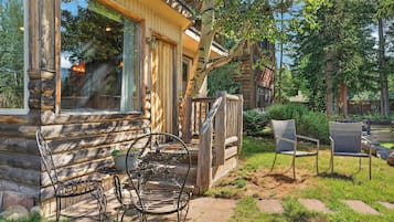 Eine Blockhütte mit Veranda, Sitzgelegenheiten im Freien und Blick auf den umliegenden Wald.