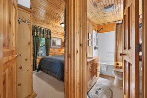 Interior de una cabaña de madera con una cama, un baño y ducha.