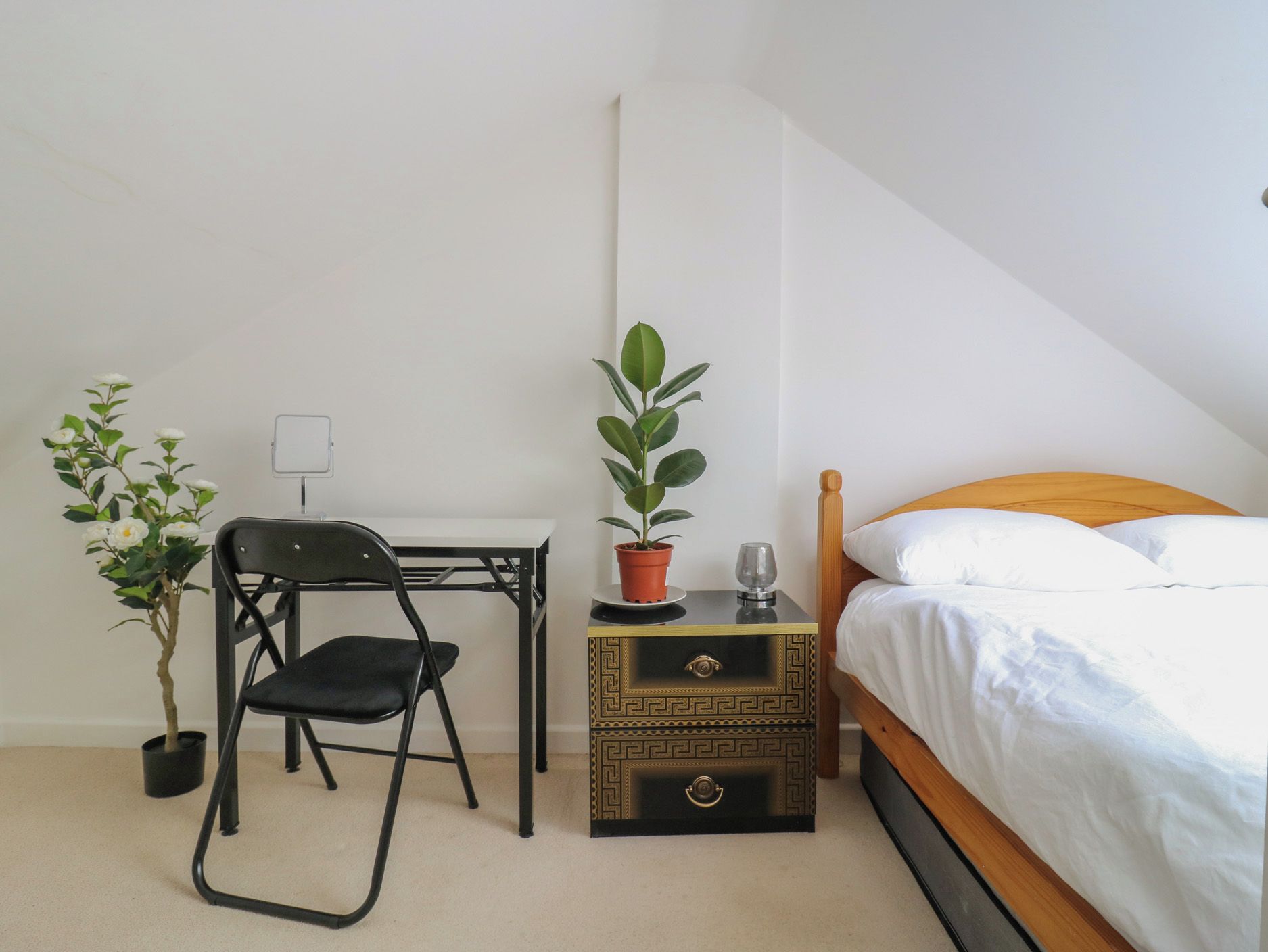 Un dormitorio con una cama, un escritorio con una silla, una planta en maceta y una mesita de noche con un vaso.
