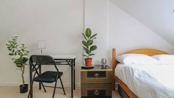 Un dormitorio con una cama, un escritorio con una silla, una planta en maceta y una mesita de noche con un vaso.
