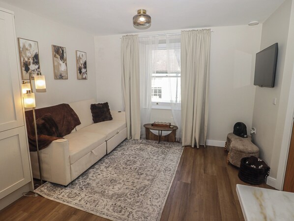 A living room with a sofa, a small round table, a television mounted on the wall, and a window with curtains.