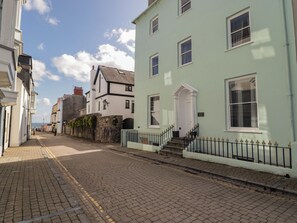 A cobblestone street lined with historic buildings, including a light green building with a white door and a stone wall with a gate.