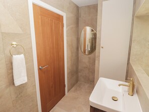 A bathroom with a wooden door, a white sink with gold fixtures, and a round mirror on the wall.