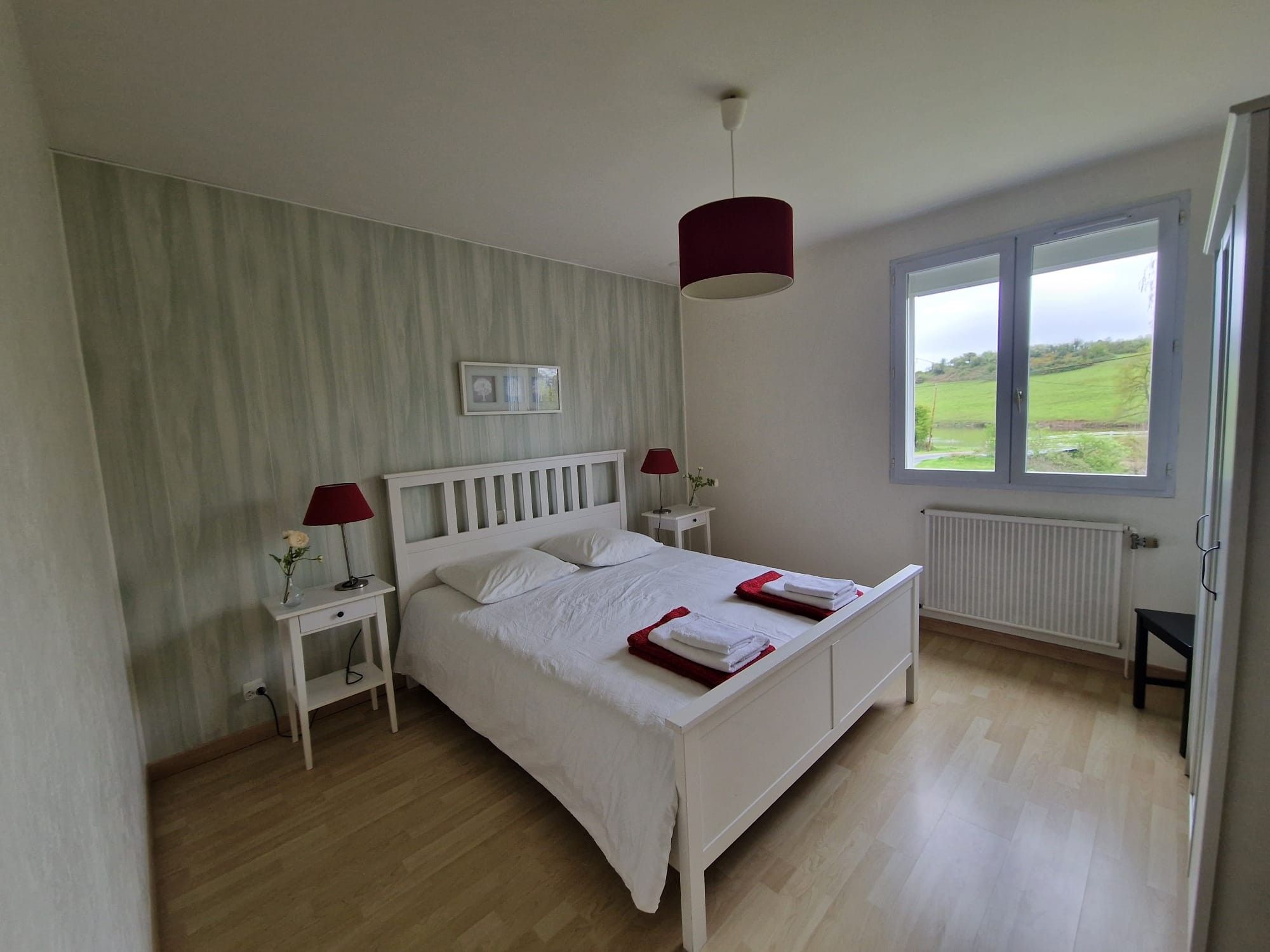 A bedroom with a bed, bedside tables, a window with a view, and a radiator.
